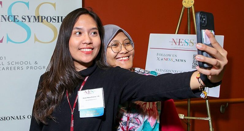 two young women taking selfie in front of event sign