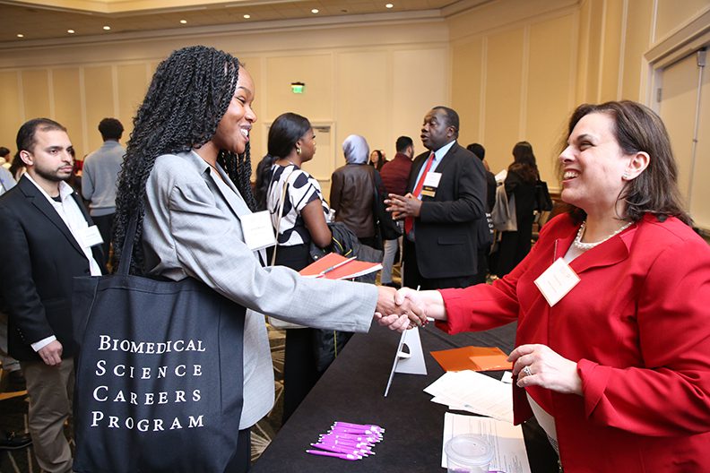 Student and conference goer shaking hands over a table