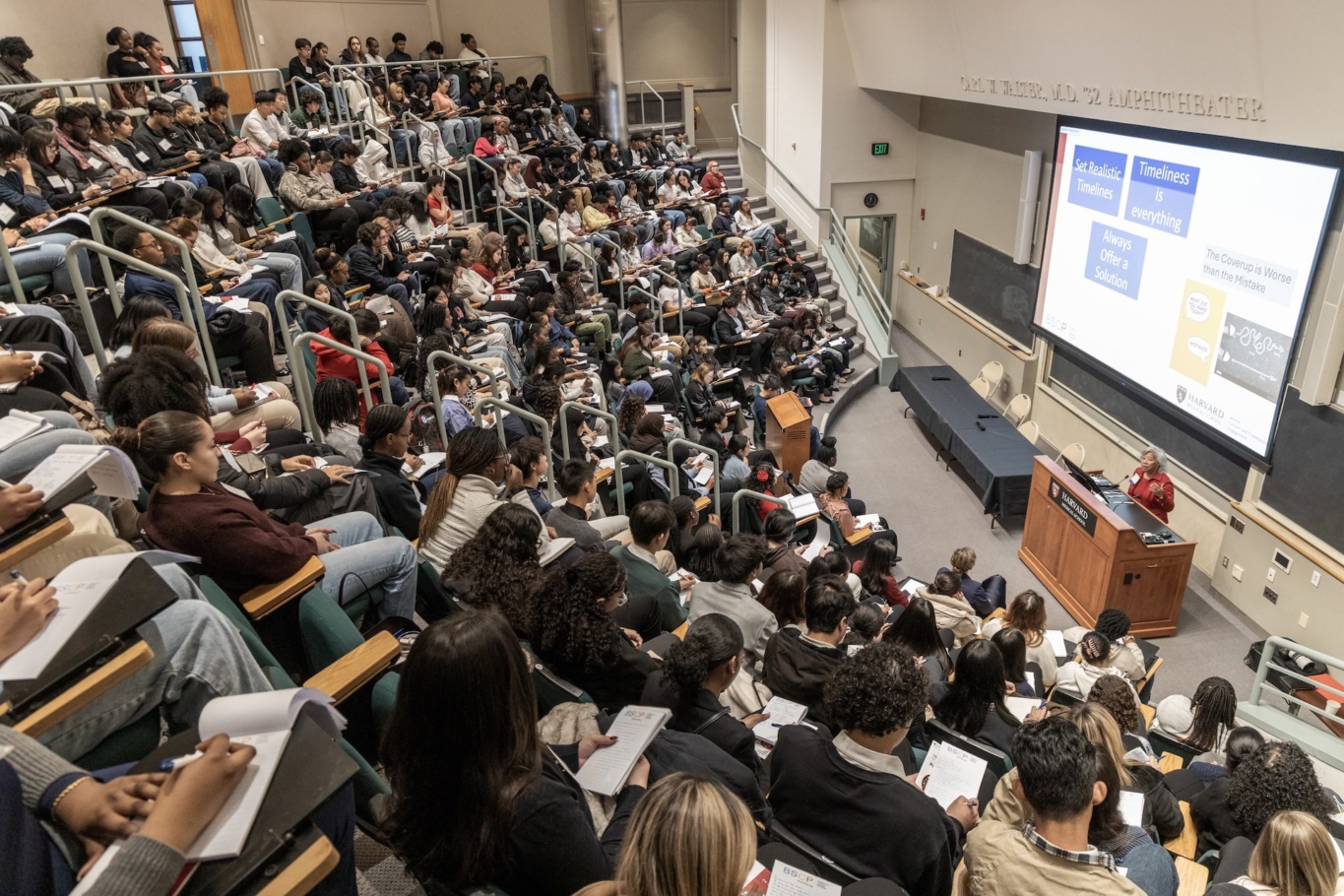 lecture hall full of students with person speaking in front of projected screen