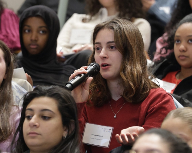 student holding microphone with other student sitting around her