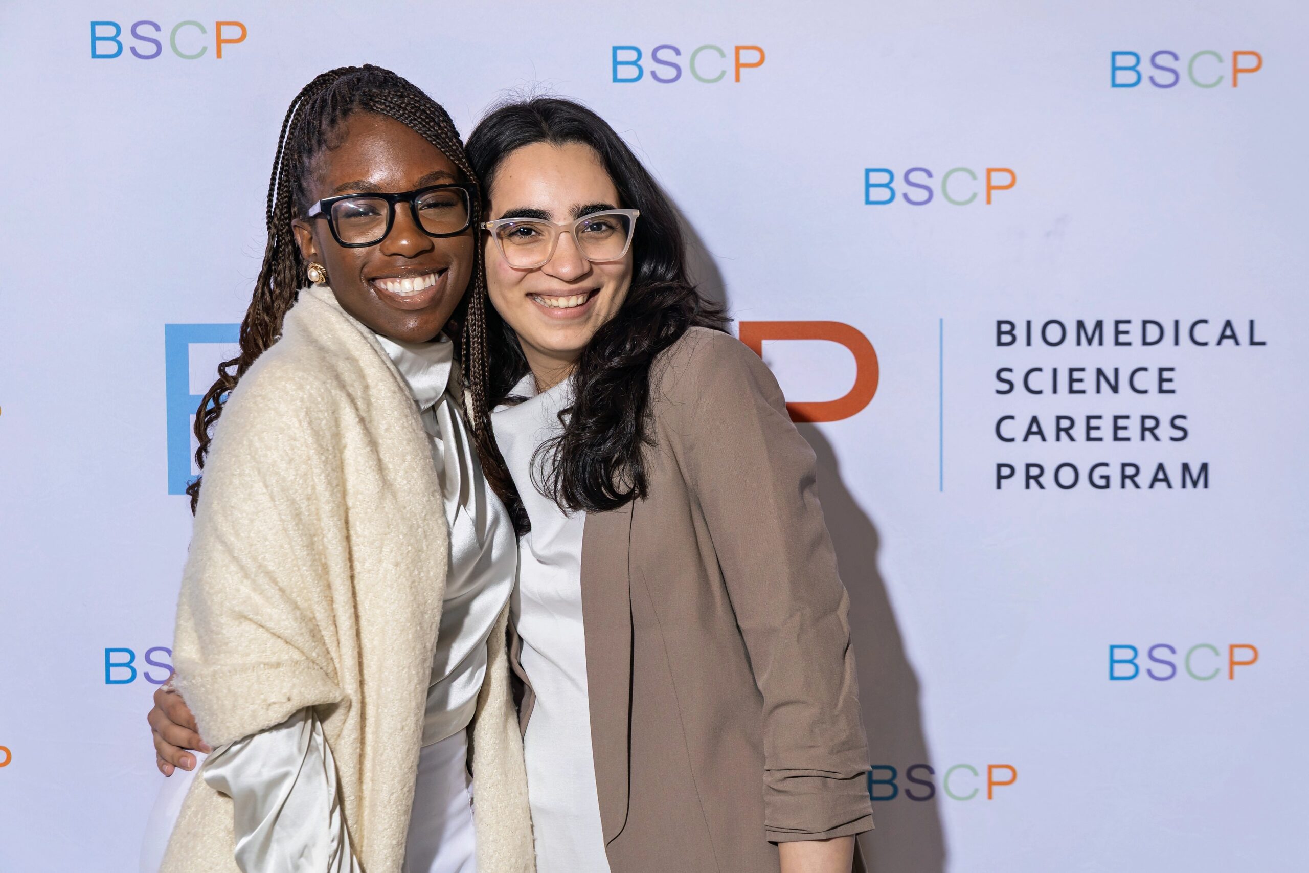 two students smiling for camera in front of BSCP step and repeat display