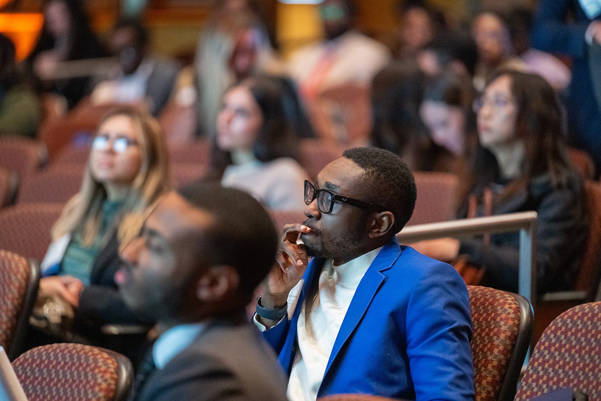 lecture hall with students listening to lecture looking forward, image focused on man in blue suite coat